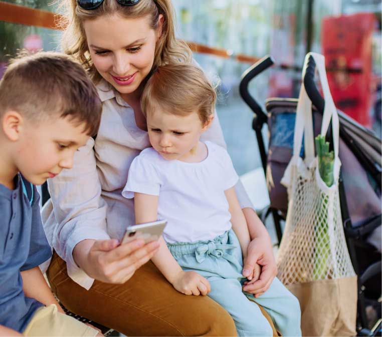 A woman sits with two children looking at a cell phone