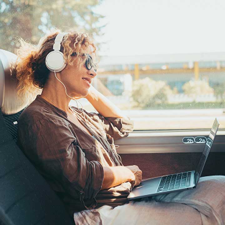 A woman wearing headphones is sitting in a bus working on her laptop